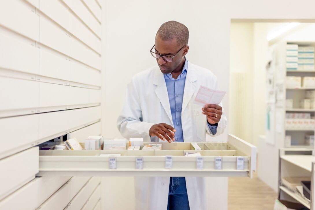 male pharmacist standing at open drawer of medications