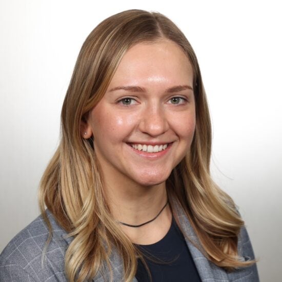 White woman with blonde hair and a grey blazer in front of a white background