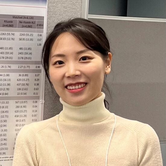 Korean woman with dark hair and tan turtleneck standing in front of an academic poster